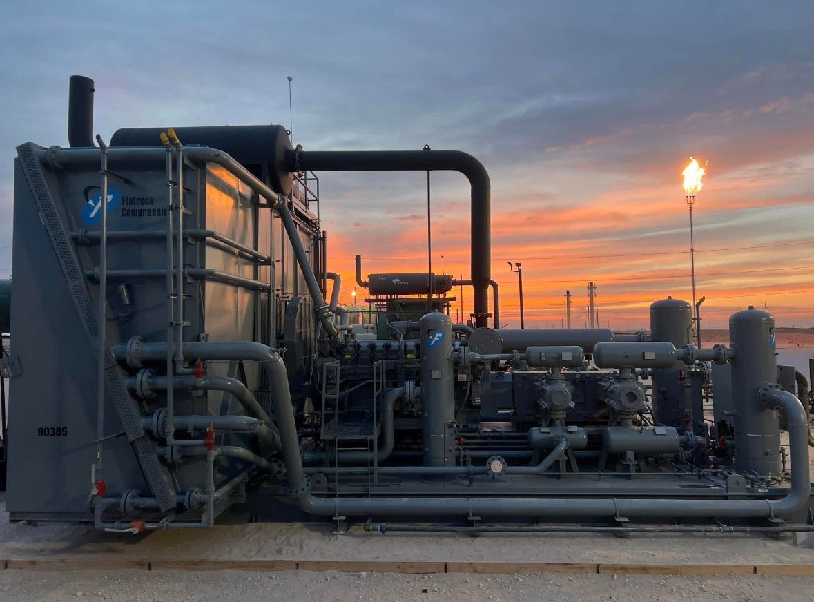 Industrial compressor station with pipes and equipment at sunset with dramatic orange sky and distant lights