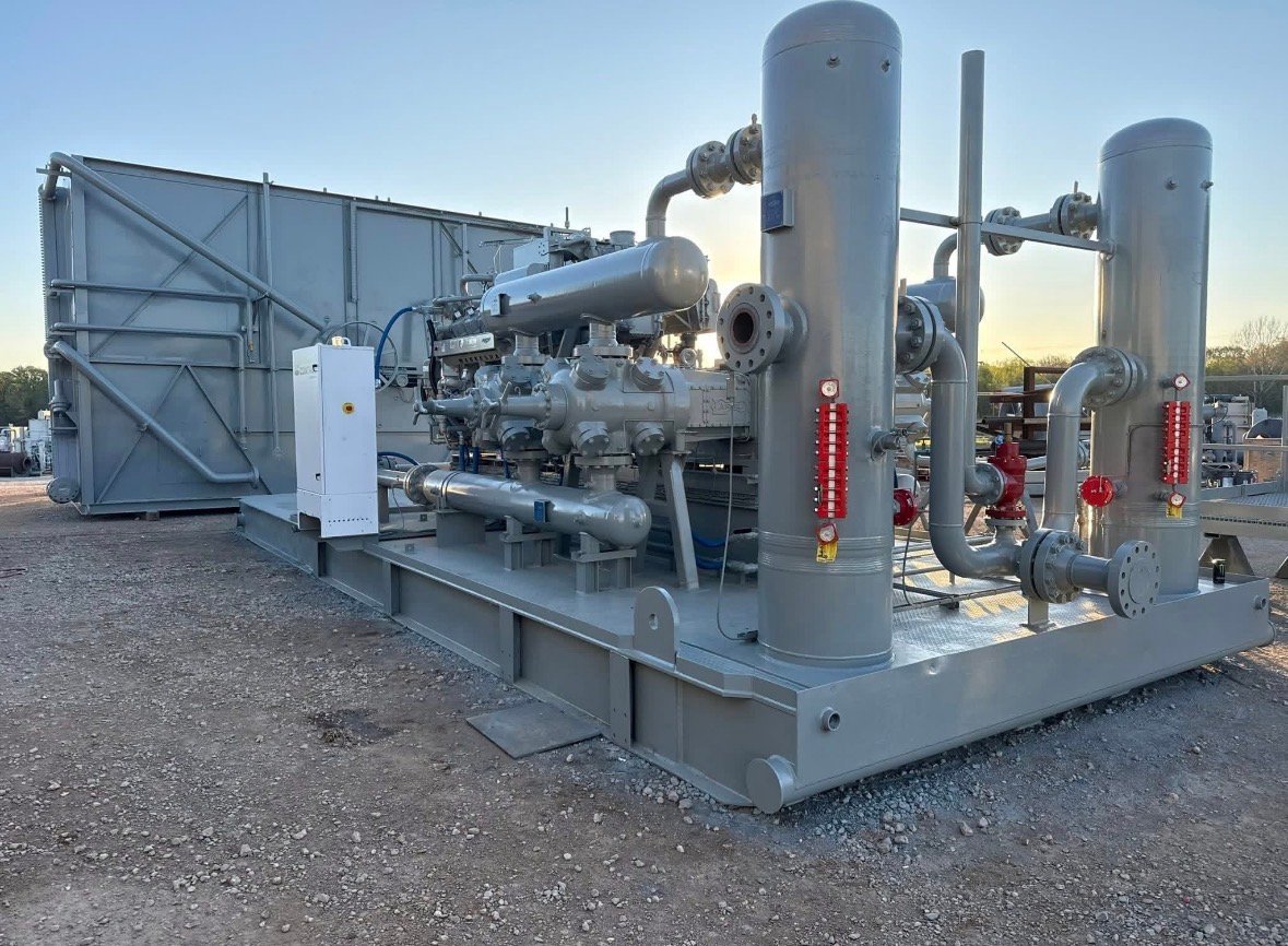 Industrial gas compression unit with engine, metal piping, and pressure tanks mounted on a concrete pad